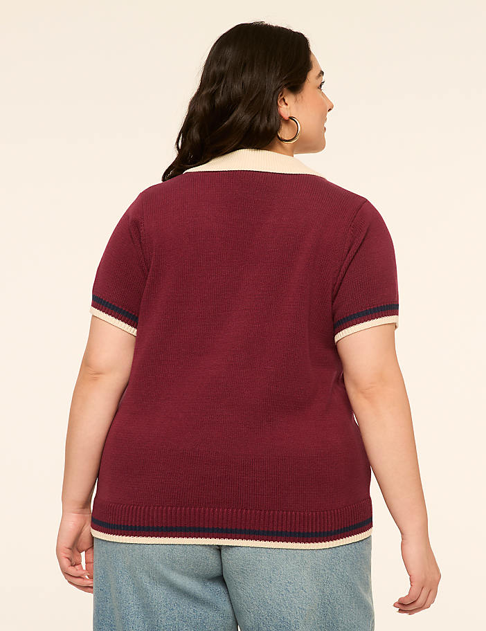 A woman in a maroon polo shirt and blue jeans stands against a plain, light-colored background.