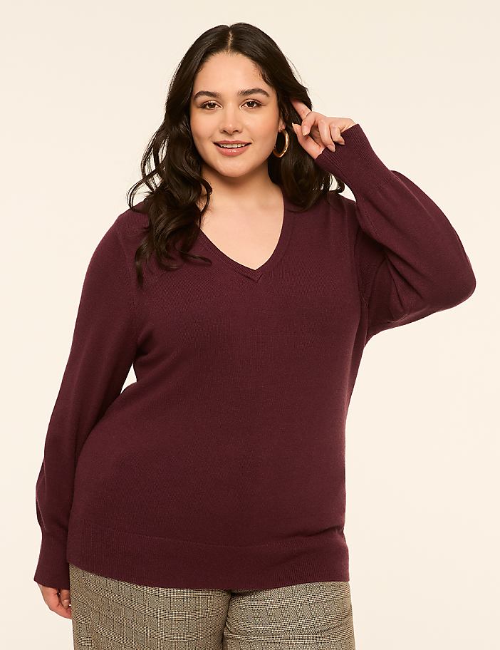 A woman in a burgundy v-neck sweater and plaid pants poses against a plain, light-colored background.