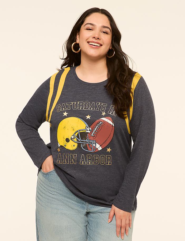 A smiling woman in a graphic t-shirt stands against a plain, light-colored background.