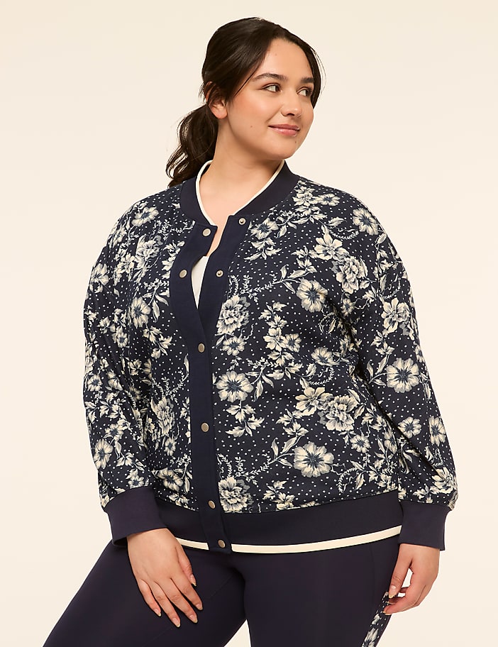 A woman in a floral bomber jacket stands against a plain, light-colored background.