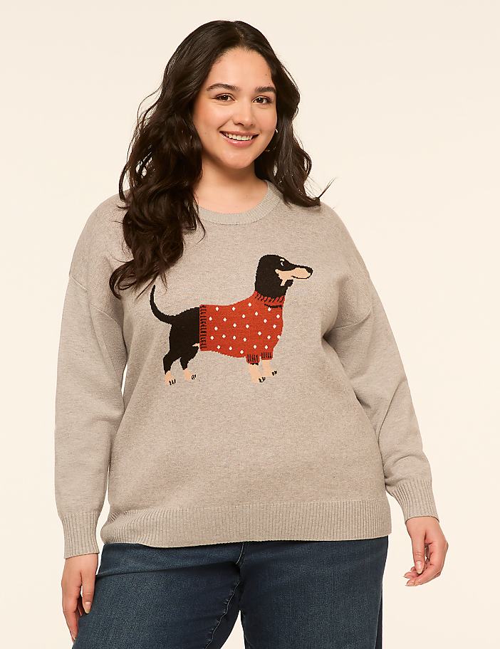 A smiling woman in a grey sweater with a dachshund graphic stands against a plain, light-colored background.