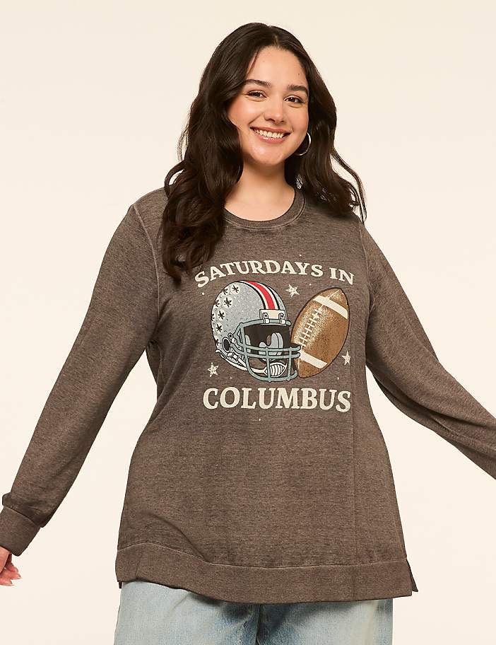 A smiling woman in a gray sweatshirt with a football graphic stands against a plain, light-colored background.