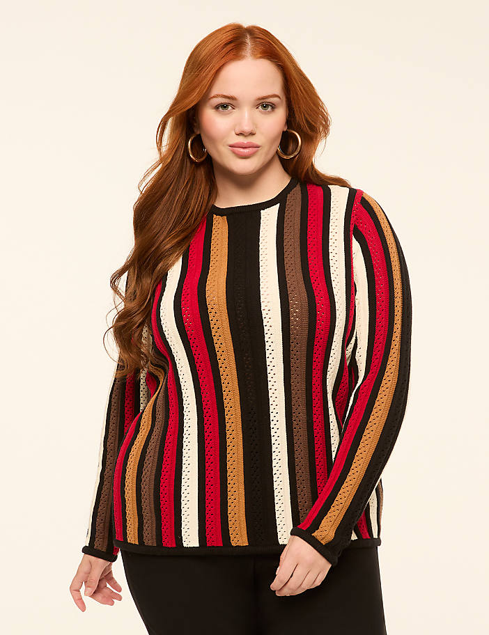 A woman with long red hair and a striped sweater stands against a plain, light-colored background.