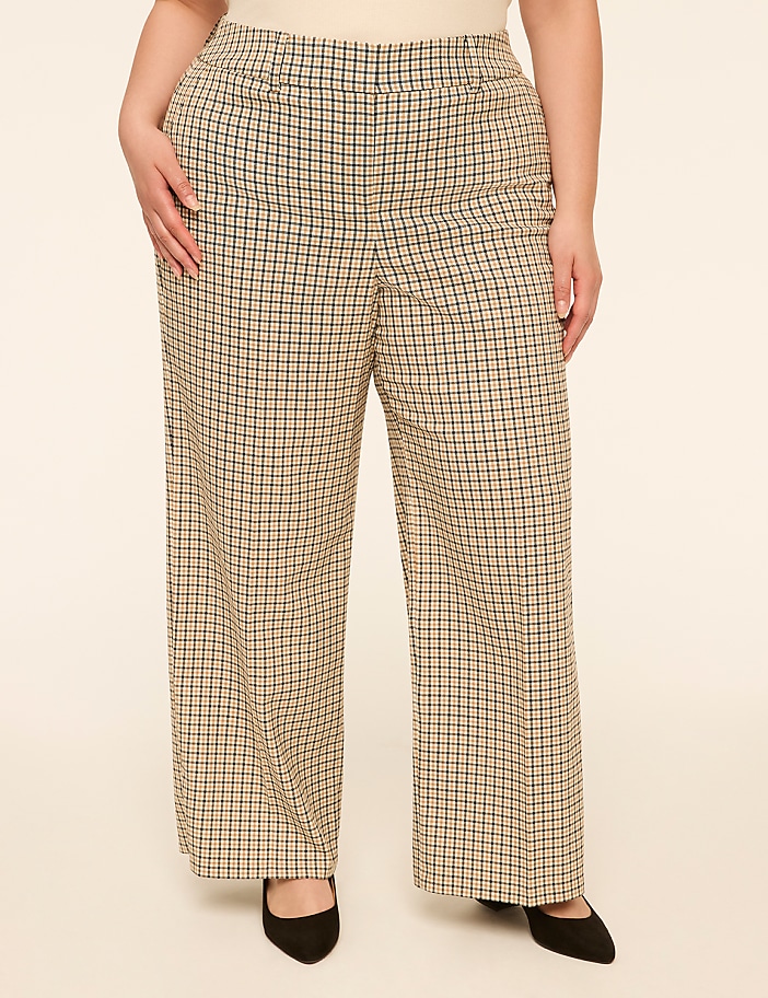 A person stands in the foreground wearing wide-leg plaid pants and black heels against a plain, light-colored background.