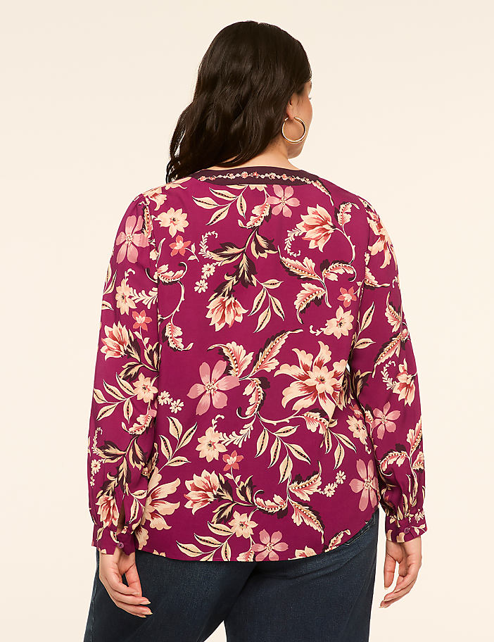 A woman in a floral print blouse stands against a plain, light-colored background.
