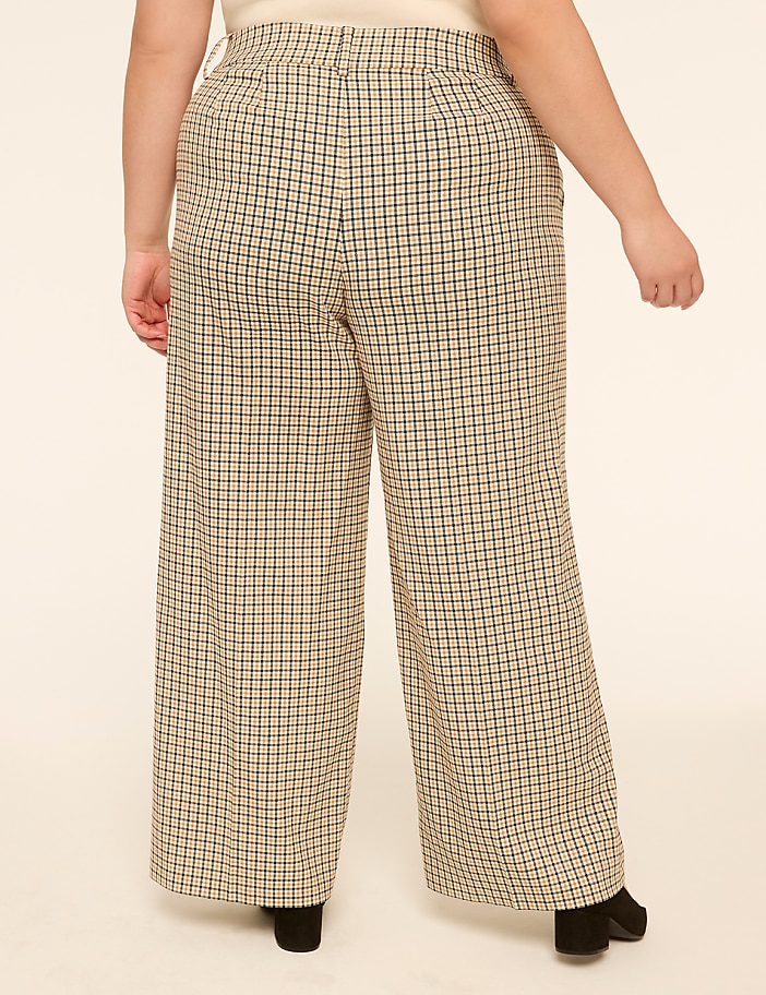 A person wearing plaid wide-leg pants stands against a plain, light-colored background.
