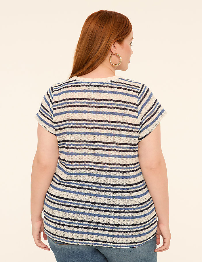 A woman with red hair, wearing a striped shirt and jeans, stands against a plain, light-colored background.