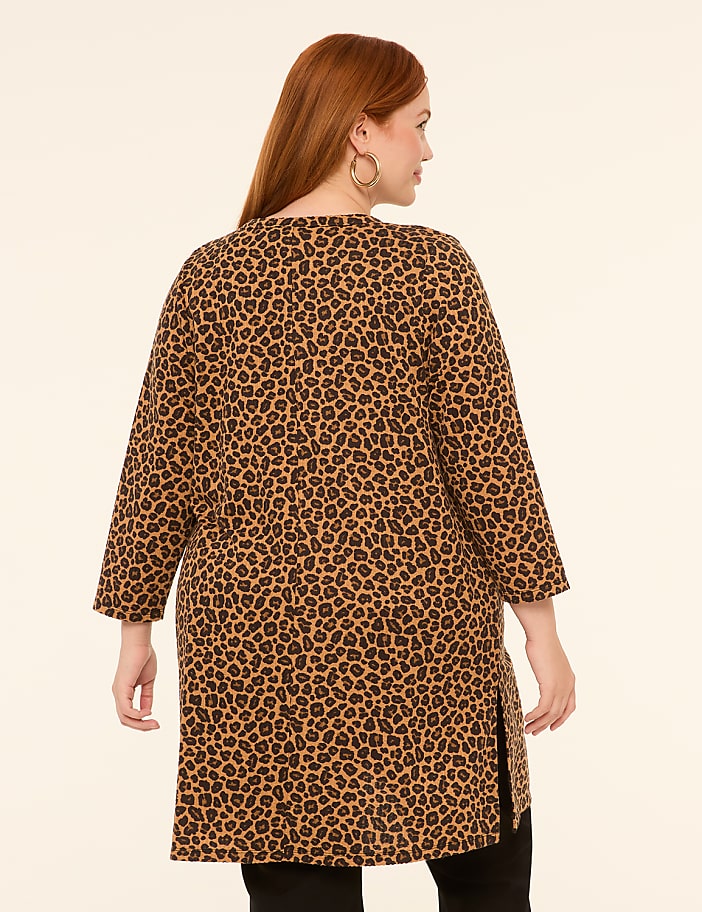 A woman with red hair wearing a leopard print tunic stands against a plain, light-colored background.