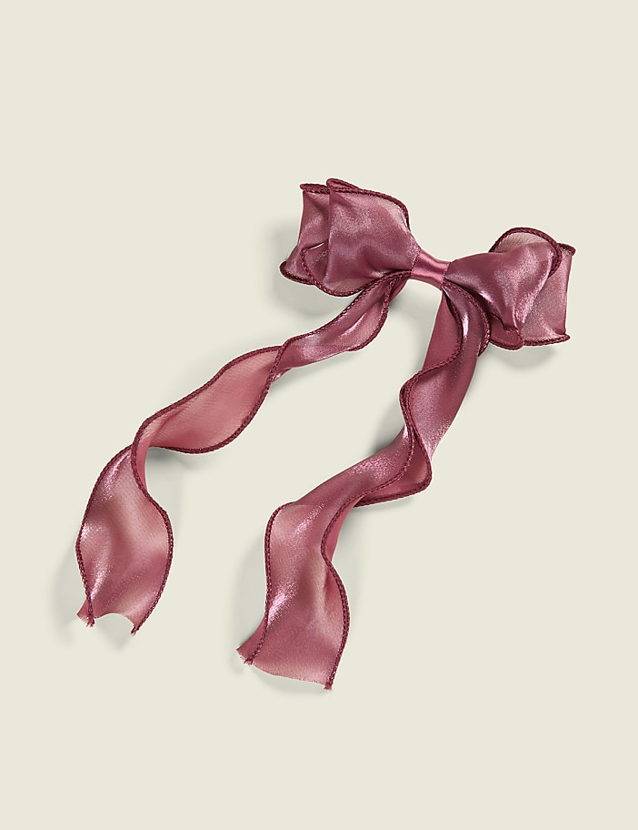 A shimmering rose-gold ribbon bow with flowing tails rests on a plain, light cream background.