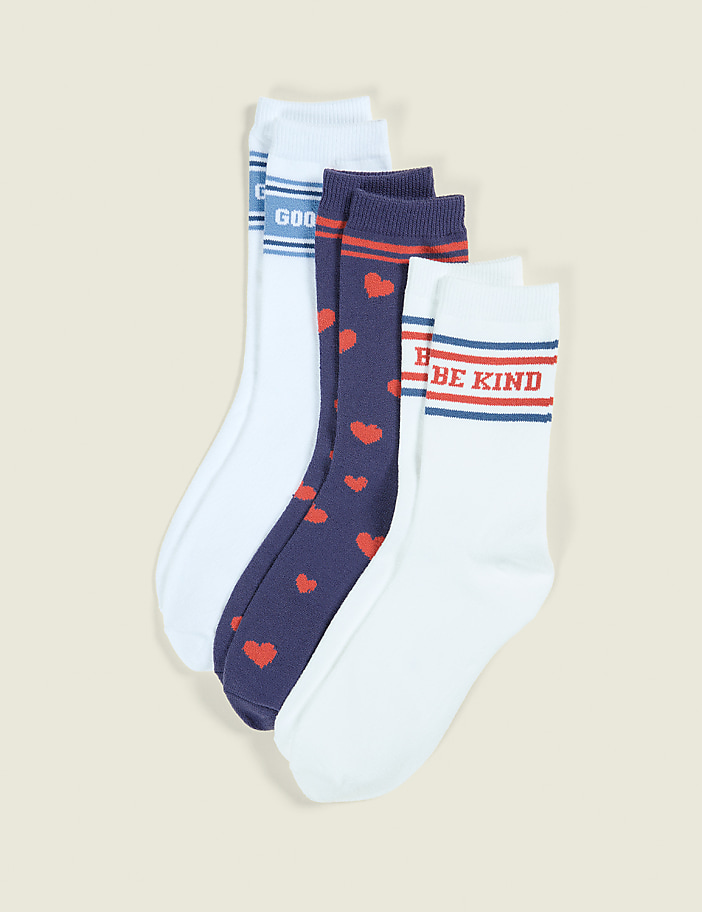 Four pairs of socks, two white with stripes and text, and two navy with red hearts, are arranged against a plain, light-colored background.