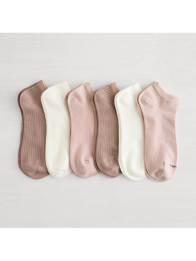 Six pairs of ribbed ankle socks in muted pink and cream hues are neatly arranged on a light, textured surface.