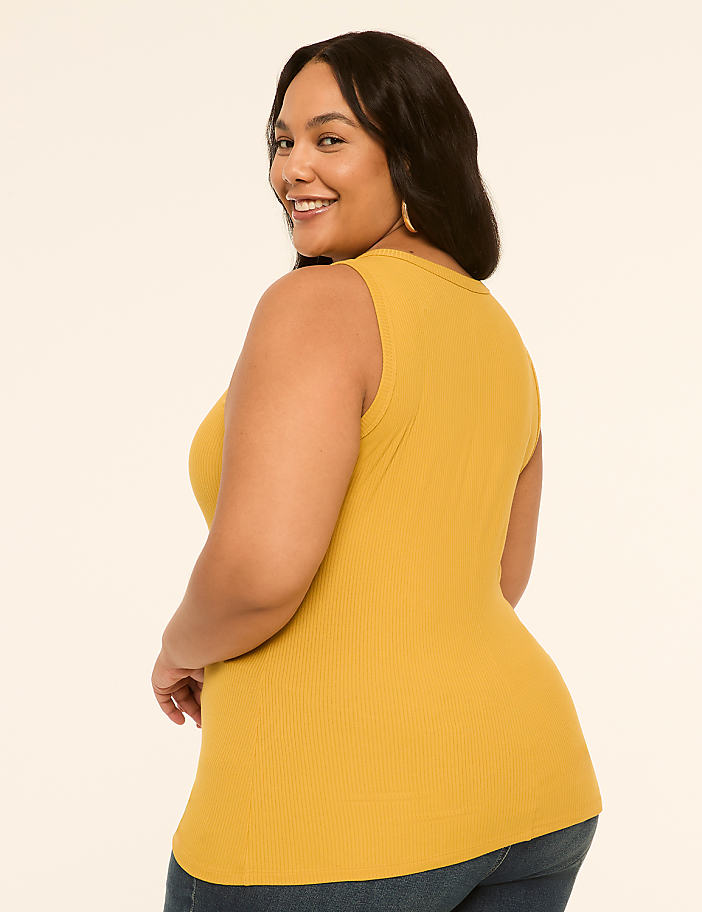 A smiling woman in a mustard yellow ribbed tank top poses against a plain, light-colored background.