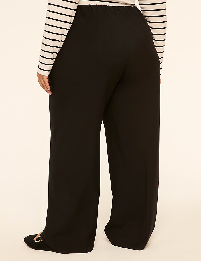 A person wearing black wide-leg pants and a striped shirt stands against a plain, light-colored background.