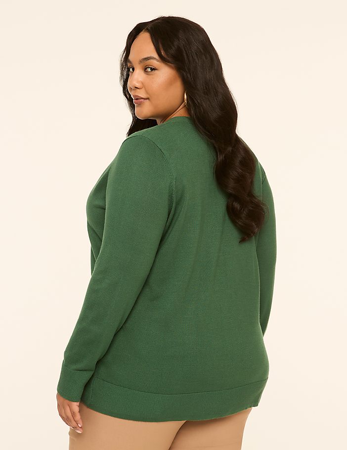 A woman in a green sweater stands against a plain, light-colored background.