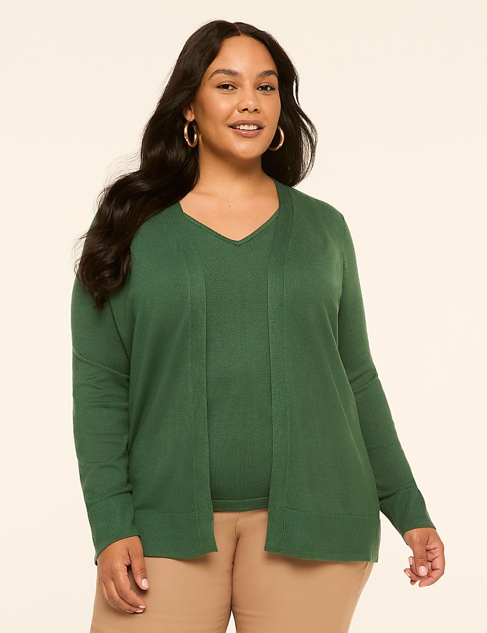 A smiling woman in a green sweater and cardigan stands against a plain, light-colored background.