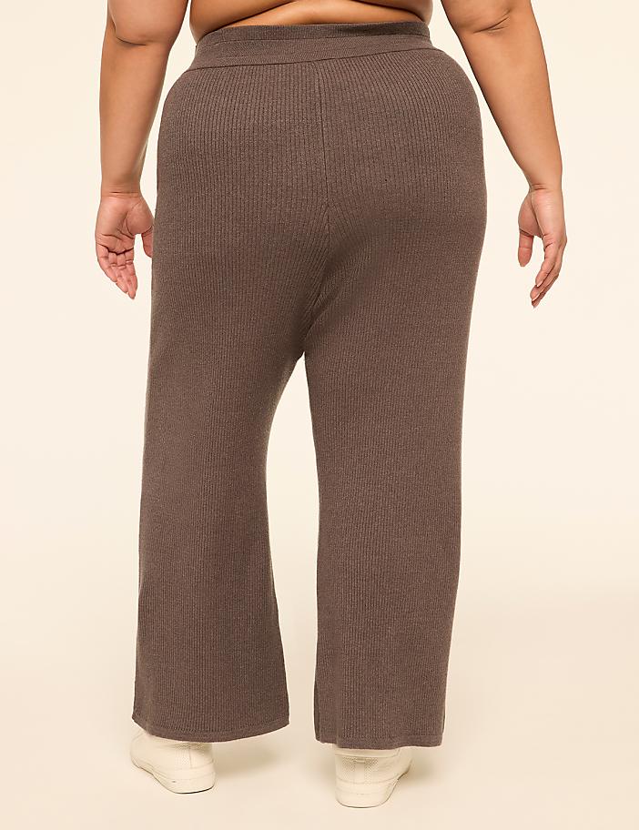 A person wearing brown knit pants and white sneakers stands against a plain beige background.