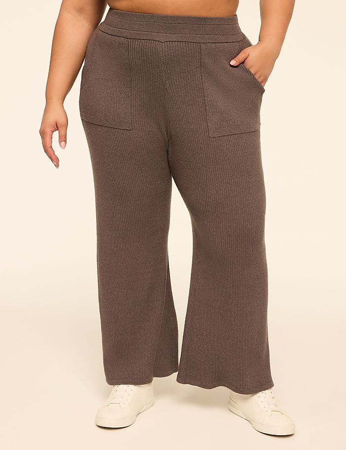 A person wearing brown ribbed knit pants with pockets and white sneakers stands against a plain beige background.