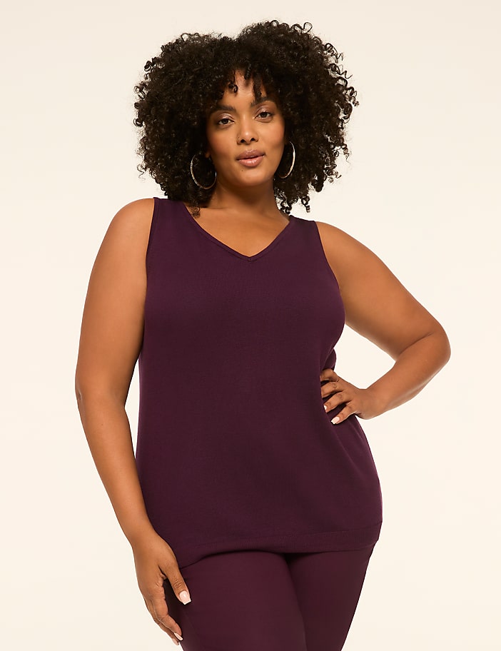 A plus-size woman in a plum-colored v-neck top and matching pants stands against a plain, light-colored background.