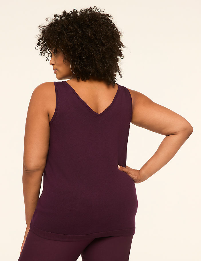 A woman in a plum-colored tank top and pants stands with her back to the viewer against a plain, light-colored background.