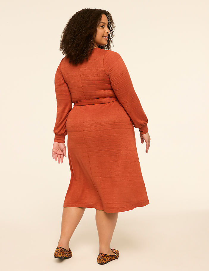 A woman in a rust-colored dress and leopard print flats stands against a plain, light-colored background.