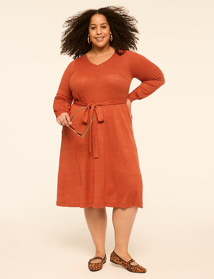 A woman in an orange dress and leopard print flats stands against a plain, light-colored background.