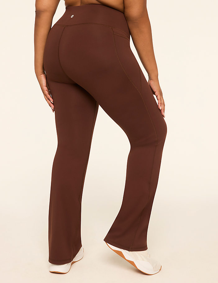 A person wearing brown flared yoga pants stands against a plain cream background.
