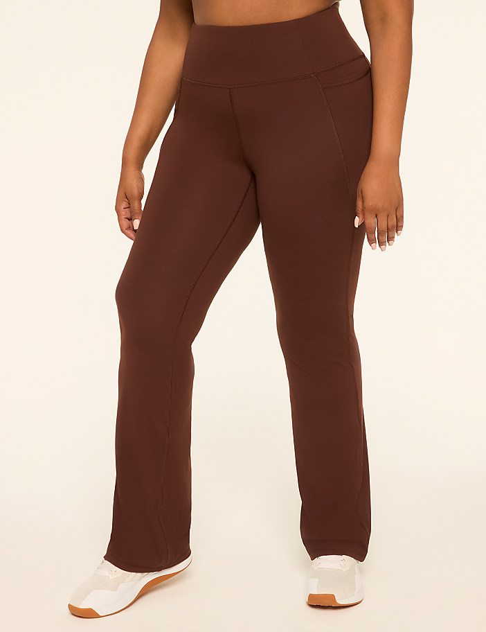 A person in brown flared yoga pants and white sneakers stands against a plain, light-colored background.