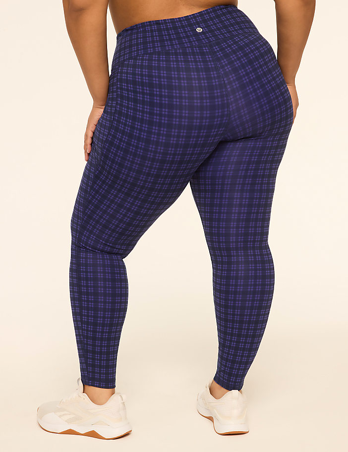 A person wearing blue plaid leggings and white sneakers stands against a plain, light-colored background.