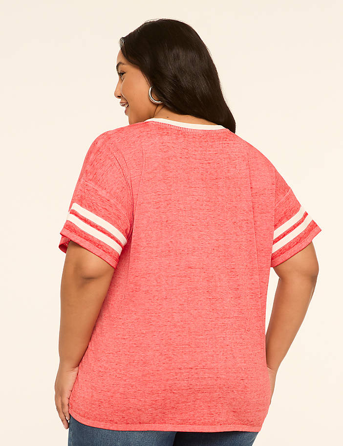 A woman in a coral t-shirt with white stripes on the sleeves stands against a plain, light-colored background.