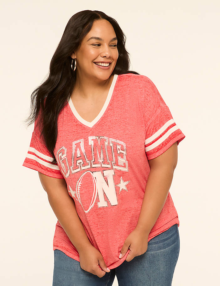 A smiling woman in a coral "GAME ON" t-shirt stands against a plain, light background.