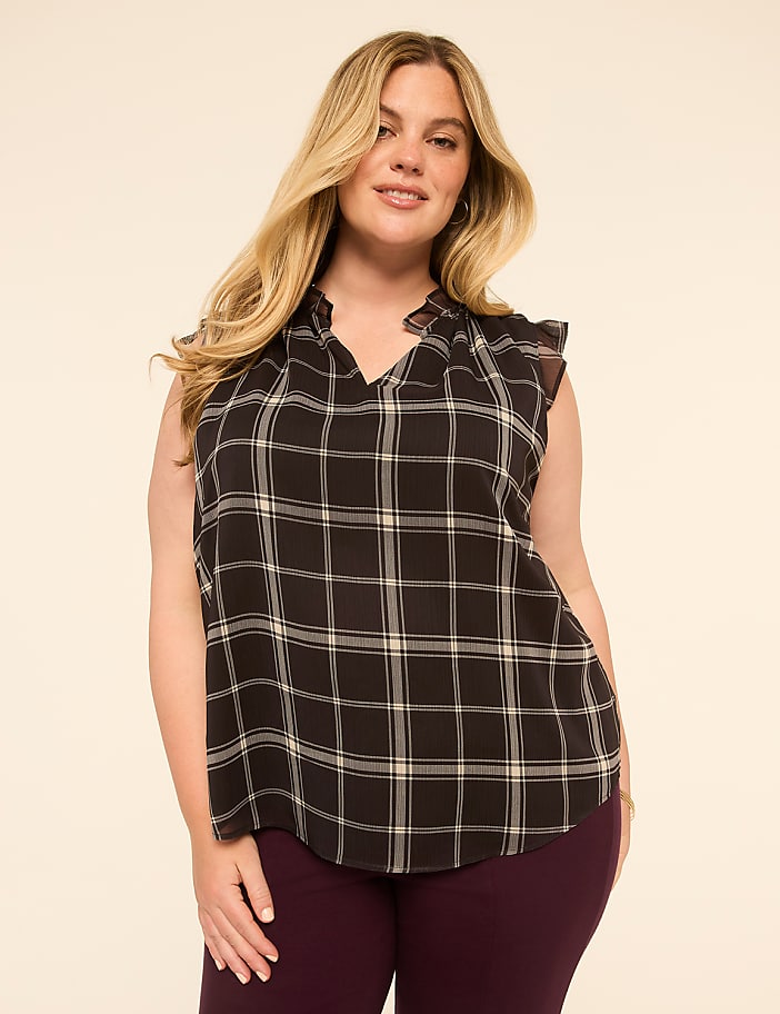 A woman with blonde hair and a plaid blouse stands against a plain, light-colored background.