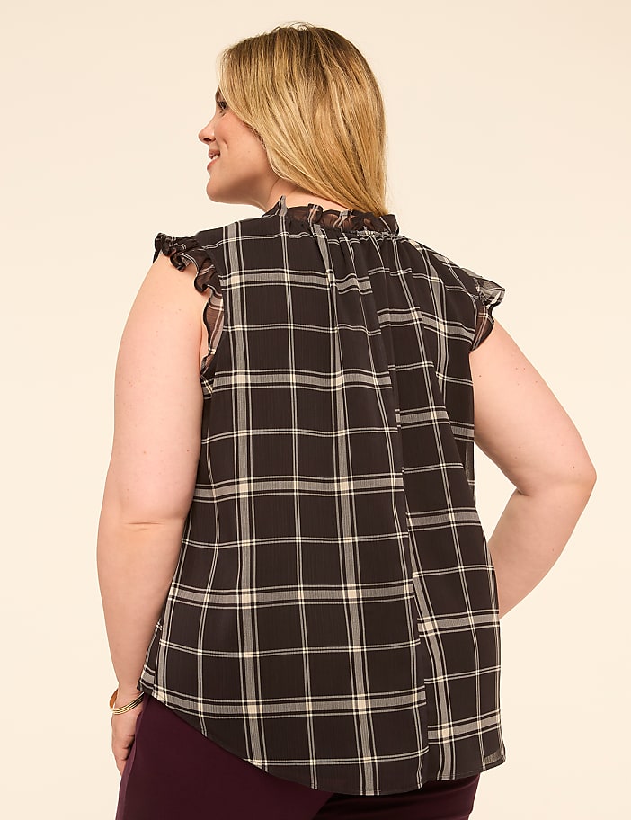 A woman in a plaid top stands against a plain, light-colored background.