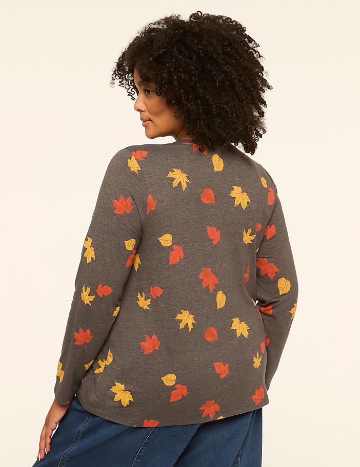 A woman in a gray sweater with a fall leaf pattern stands against a plain, light-colored background.
