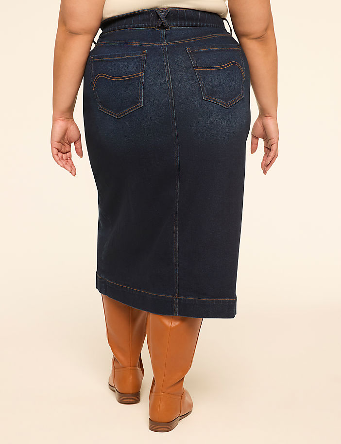 A person wearing a dark denim skirt and brown boots stands against a plain, light-colored background.