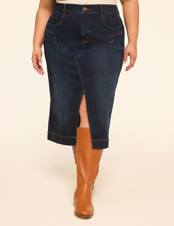 A woman in a dark denim skirt and brown boots stands against a plain, light-colored background.