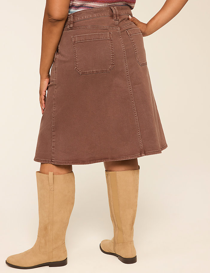 A person wearing a brown denim skirt and tan boots stands against a plain, light-colored background.