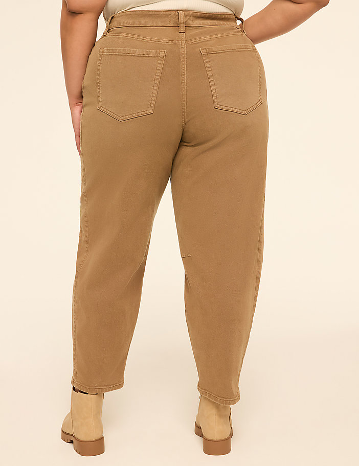 A person wearing tan jeans and boots stands against a plain, light-colored background.