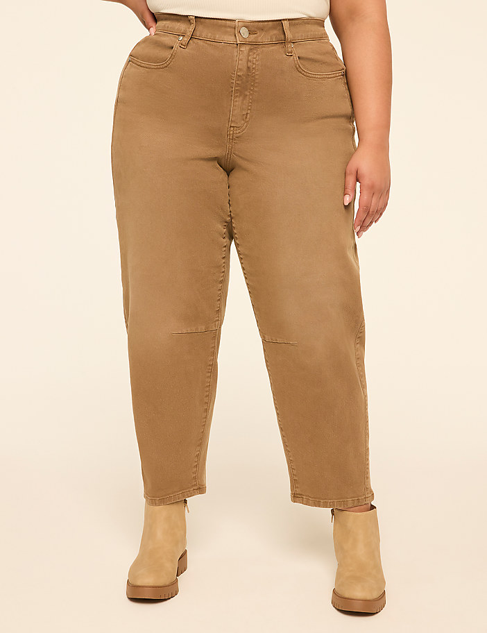A person stands in the foreground wearing brown jeans and tan boots against a plain, light-colored background.
