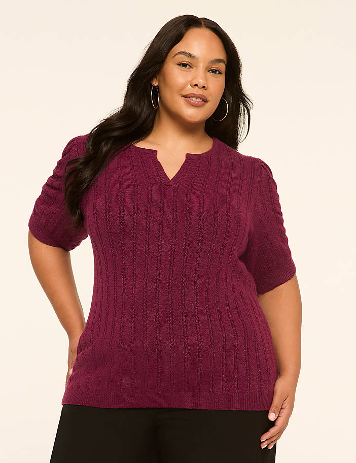 A woman in a plum-colored sweater stands against a plain, light-colored background.