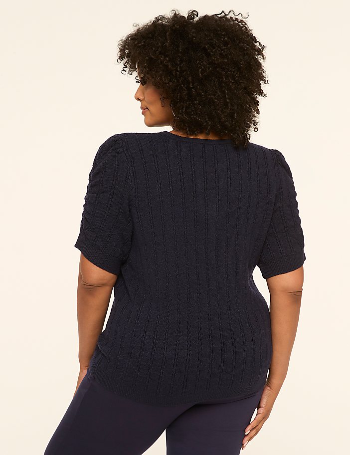 A woman in a navy blue sweater and pants stands against a plain, light-colored background.