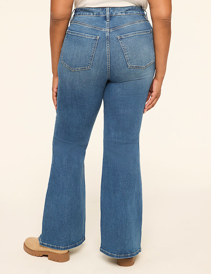 A person wearing flared denim jeans stands against a plain, light-colored background.