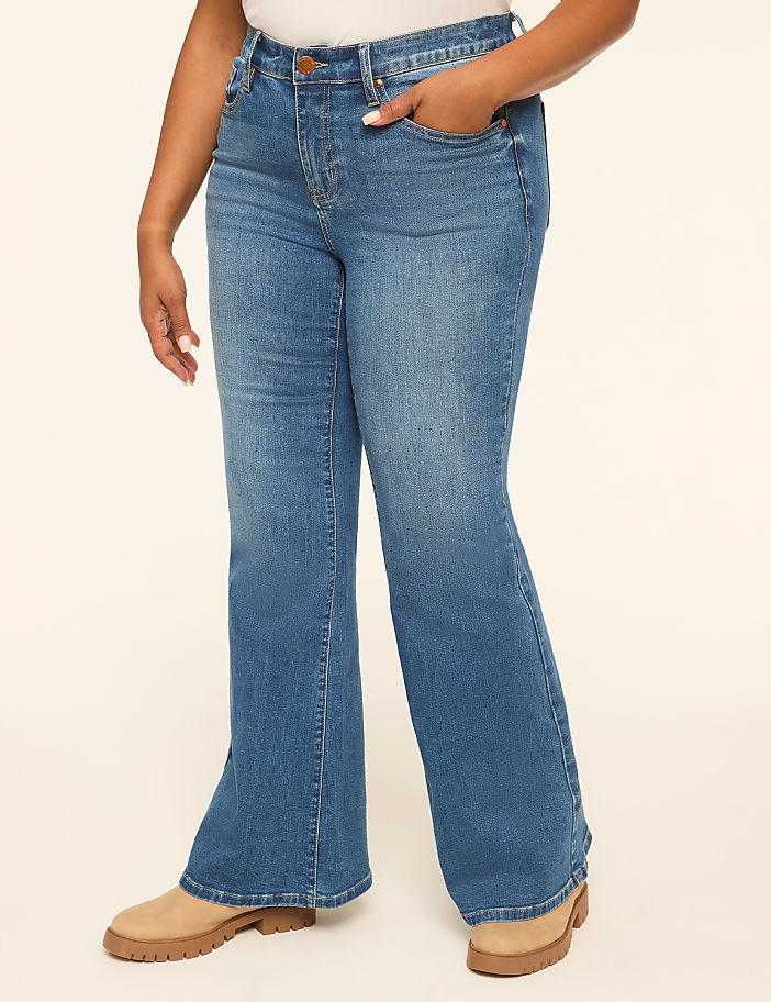 A person in flared blue jeans and tan boots stands against a plain, light-colored background.
