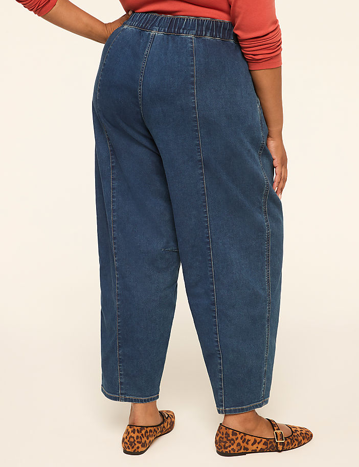 A person wearing loose-fitting denim pants and leopard print flats stands against a plain, light-colored background.