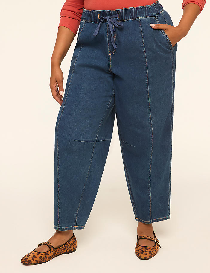 A person wearing loose-fitting denim pants and leopard print flats stands against a plain, light-colored background.