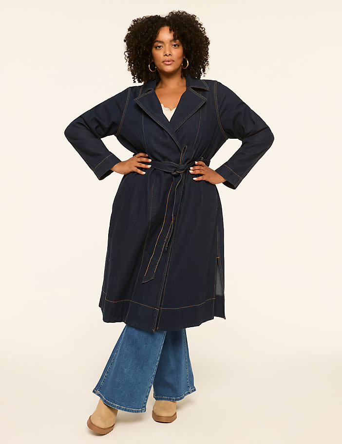 A woman in a denim trench coat and wide-leg jeans poses against a plain, light-colored background.