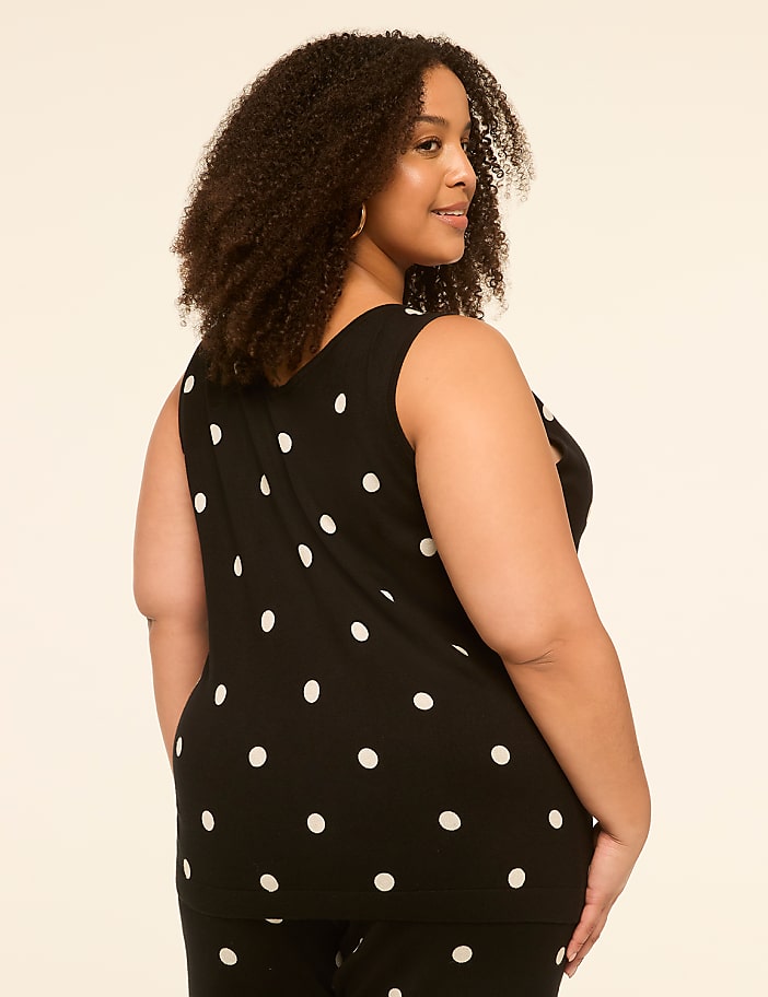 A woman with curly hair in a black and white polka dot top stands against a plain, light-colored background.