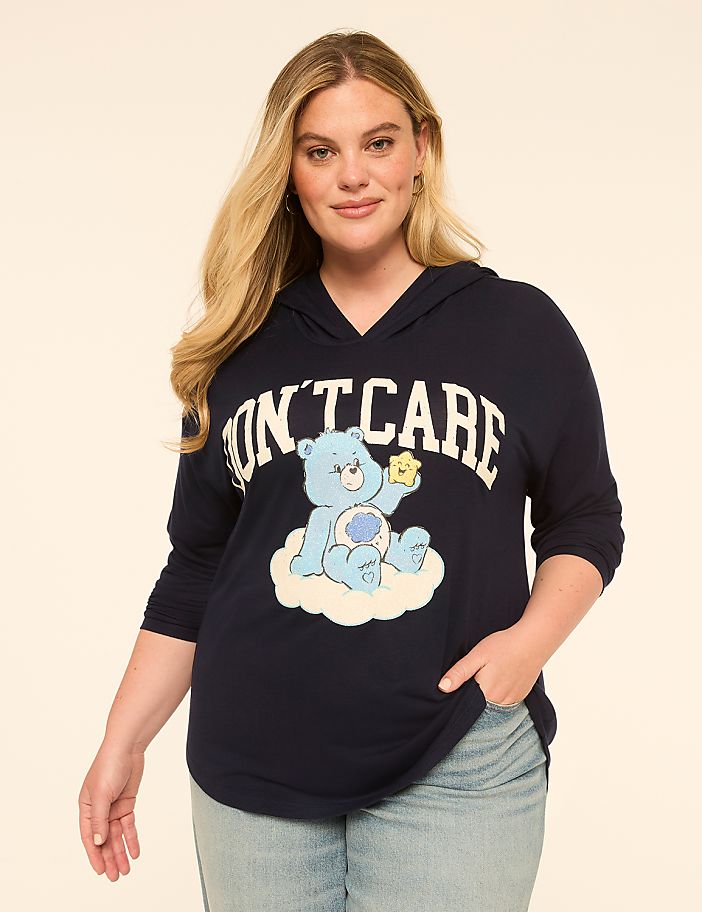 A woman in a navy blue hoodie with a Care Bear graphic stands against a plain, light-colored background.