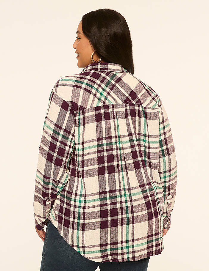 A woman in a plaid shirt stands against a plain, light-colored background.