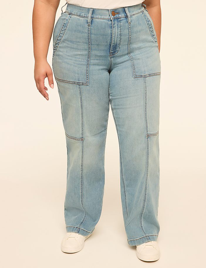 A person stands in light-wash denim jeans with prominent stitching and large front pockets, against a plain, light-colored background.