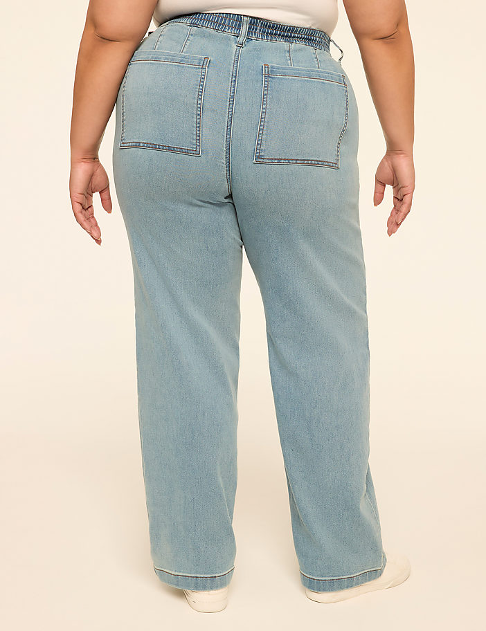 A person wearing light blue wide-leg jeans stands against a plain, light-colored background.